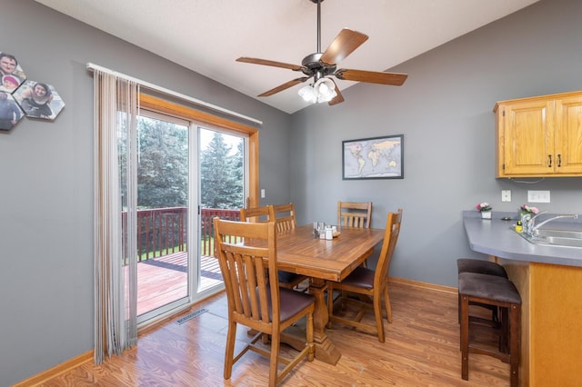 dining space with ceiling fan, sink, light hardwood / wood-style floors, and vaulted ceiling