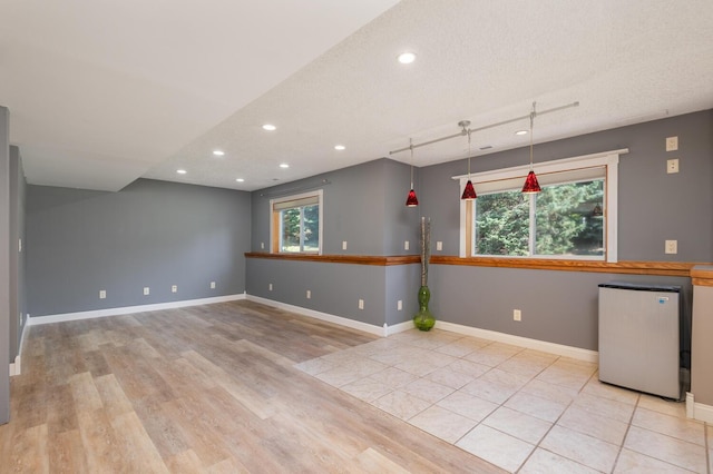 empty room with a textured ceiling, a wealth of natural light, light tile patterned floors, and track lighting