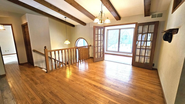 empty room featuring beam ceiling, hardwood / wood-style floors, a chandelier, and french doors