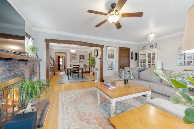 living room featuring a ceiling fan, a fireplace, crown molding, and light wood finished floors