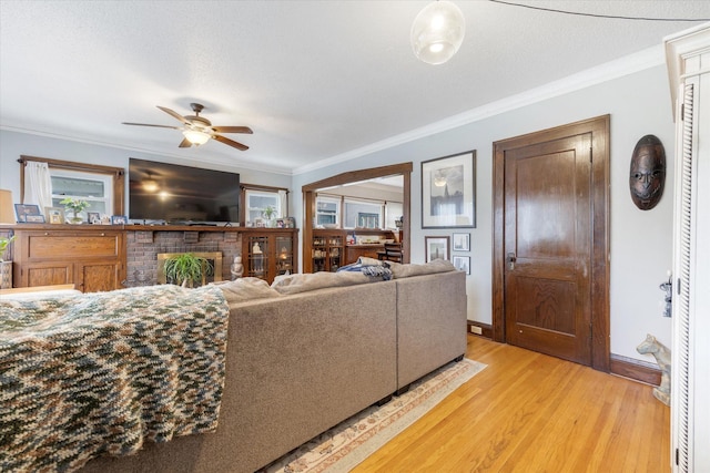 living room with a brick fireplace, ceiling fan, baseboards, light wood-type flooring, and ornamental molding