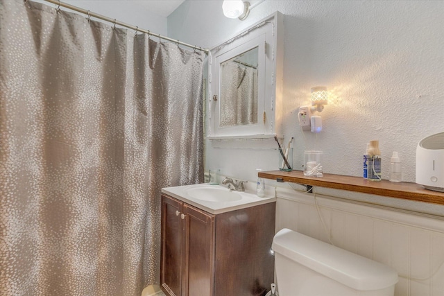 full bathroom with curtained shower, toilet, vanity, and a textured wall