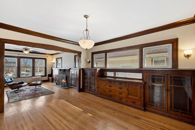 living room with radiator, wood finished floors, a warm lit fireplace, and ornamental molding