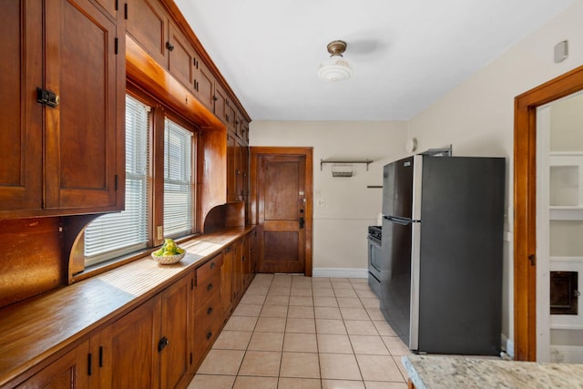 kitchen with light countertops, light tile patterned floors, gas stove, and freestanding refrigerator