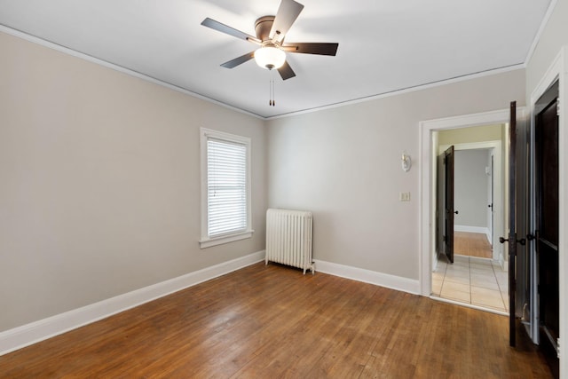 empty room with ceiling fan, baseboards, radiator heating unit, ornamental molding, and hardwood / wood-style flooring