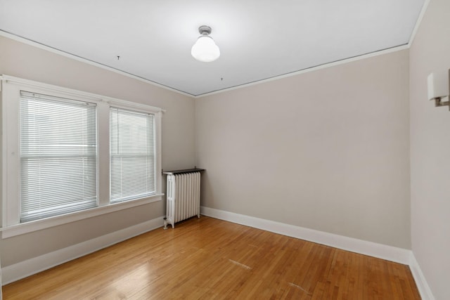 empty room with light wood-type flooring, baseboards, radiator, and ornamental molding