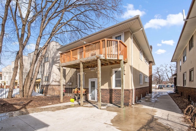 view of front of home with brick siding, stucco siding, a deck, and fence