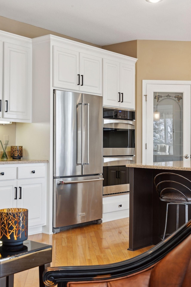 kitchen featuring stainless steel appliances, white cabinetry, and light stone counters