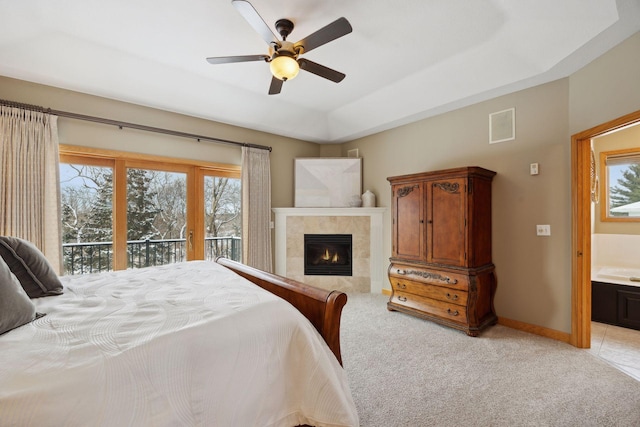 carpeted bedroom with ceiling fan, access to exterior, ensuite bathroom, a tray ceiling, and a tiled fireplace