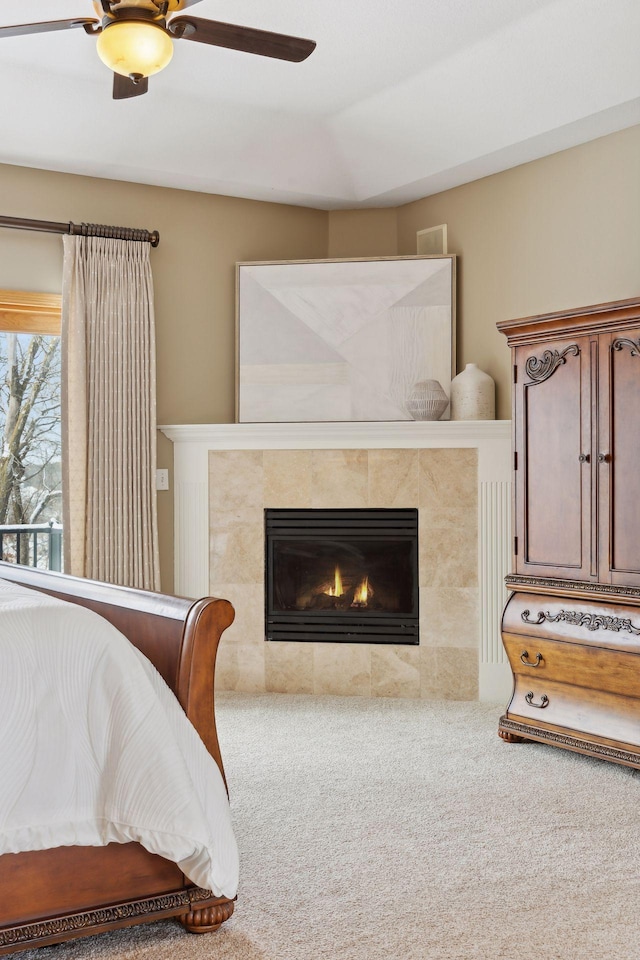 bedroom with a tiled fireplace, ceiling fan, and carpet flooring