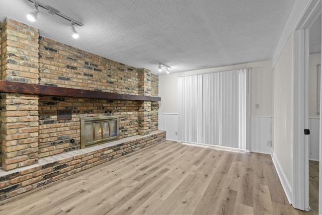 unfurnished living room featuring a brick fireplace, a textured ceiling, and light wood-type flooring