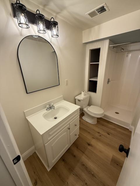 bathroom with wood-type flooring, toilet, vanity, and a shower