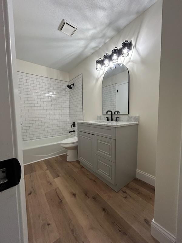 full bathroom featuring vanity, hardwood / wood-style flooring, tiled shower / bath combo, and toilet