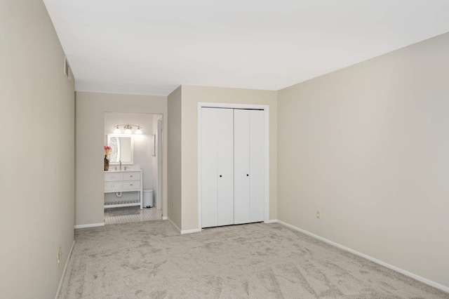 unfurnished bedroom with light colored carpet, ensuite bathroom, and a closet