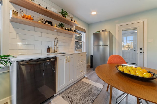 kitchen with white cabinets, sink, light wood-type flooring, tasteful backsplash, and stainless steel appliances