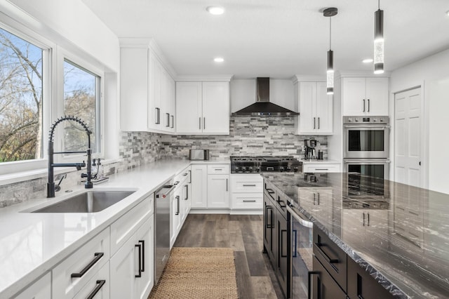 kitchen featuring appliances with stainless steel finishes, wall chimney exhaust hood, sink, decorative light fixtures, and white cabinetry