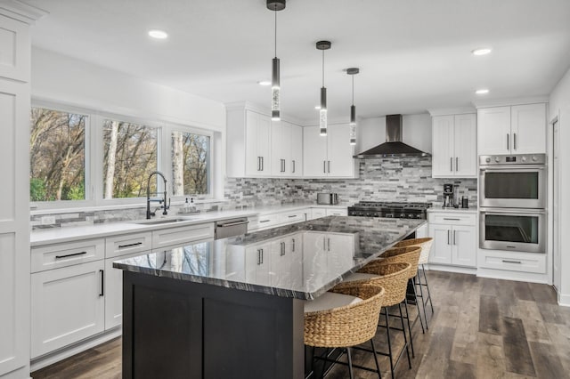 kitchen featuring a center island, stainless steel appliances, white cabinetry, and wall chimney range hood