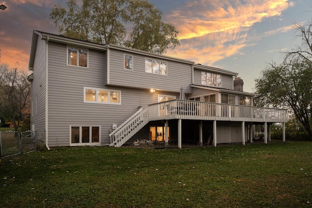 back house at dusk featuring a lawn and a deck