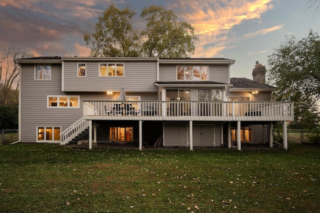 back house at dusk featuring a yard, a deck, and a sunroom