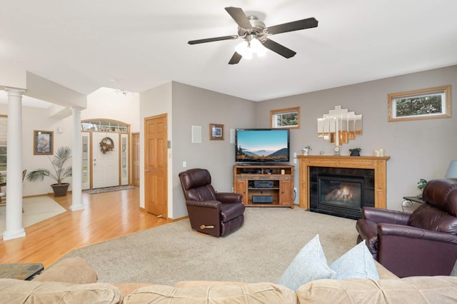 living room featuring light wood-type flooring, ornate columns, ceiling fan, and a tiled fireplace