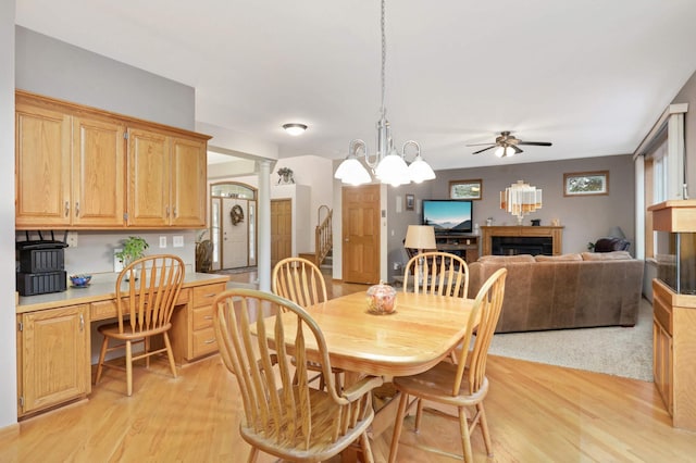 dining space with decorative columns, ceiling fan with notable chandelier, and light wood-type flooring