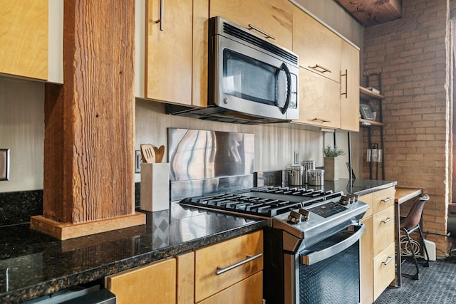 kitchen with stainless steel appliances, dark tile patterned floors, dark stone counters, and brick wall