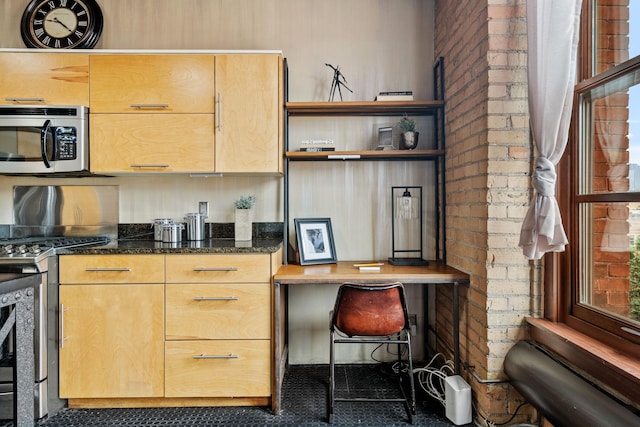 kitchen with brick wall, dark stone countertops, and appliances with stainless steel finishes