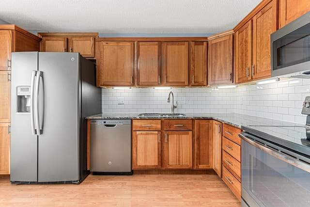 kitchen with sink, stone counters, stainless steel appliances, light hardwood / wood-style floors, and backsplash