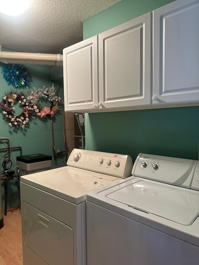 laundry area featuring washing machine and dryer, cabinets, a textured ceiling, and light wood-type flooring