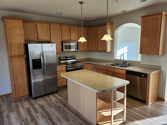 kitchen with pendant lighting, a center island, sink, light wood-type flooring, and appliances with stainless steel finishes