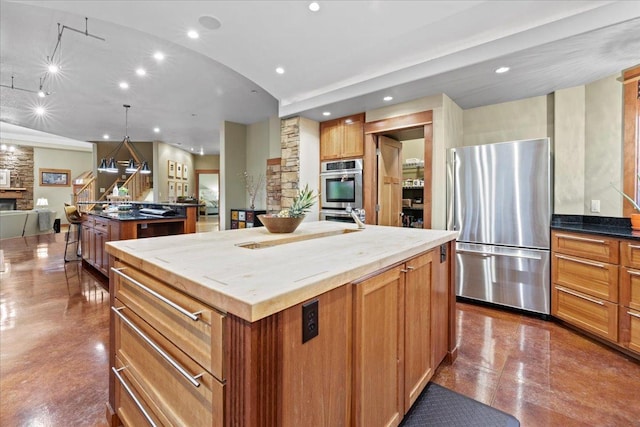 kitchen with decorative light fixtures, stainless steel appliances, dark stone counters, a fireplace, and a large island