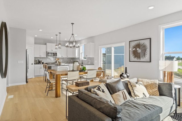 living room featuring light hardwood / wood-style floors, an inviting chandelier, a wealth of natural light, and sink