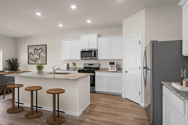 kitchen with a breakfast bar, a sink, light wood-style floors, white cabinets, and appliances with stainless steel finishes