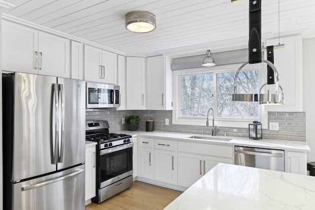 kitchen with white cabinetry, sink, stainless steel appliances, light stone counters, and light hardwood / wood-style floors