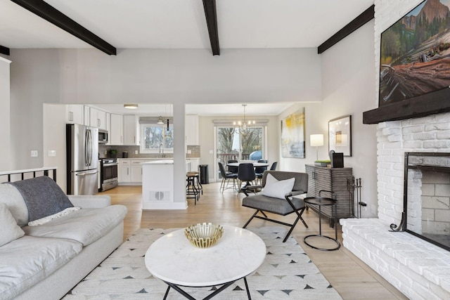 living room with a chandelier, beam ceiling, light hardwood / wood-style flooring, and a brick fireplace