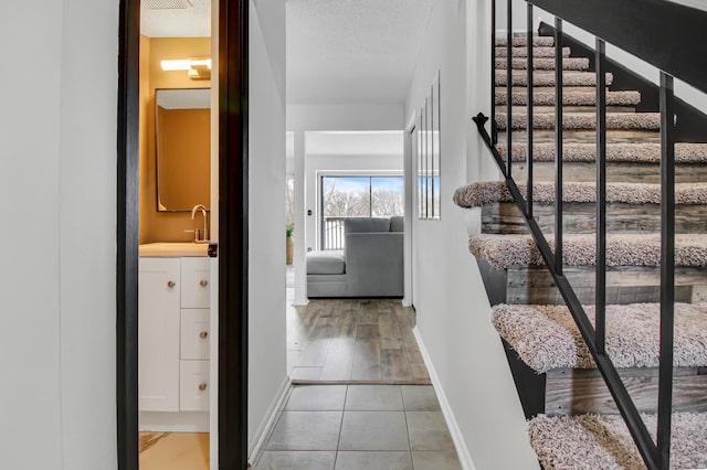 stairs with tile patterned flooring, sink, and a textured ceiling