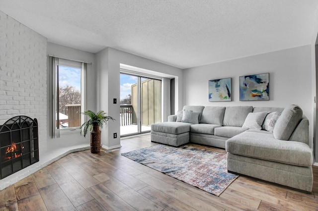 living area featuring a brick fireplace, a textured ceiling, baseboards, and wood finished floors