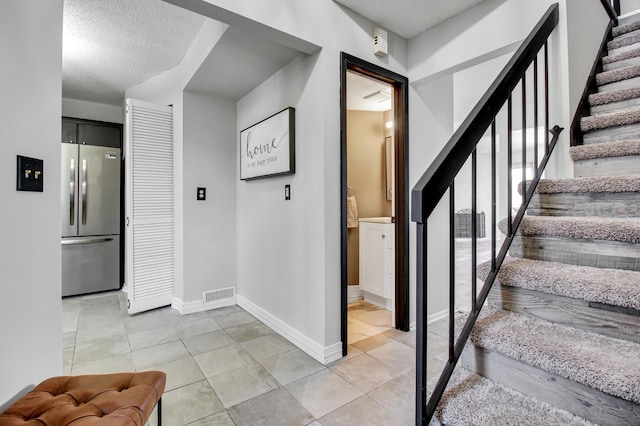 staircase with a textured ceiling, tile patterned floors, visible vents, and baseboards