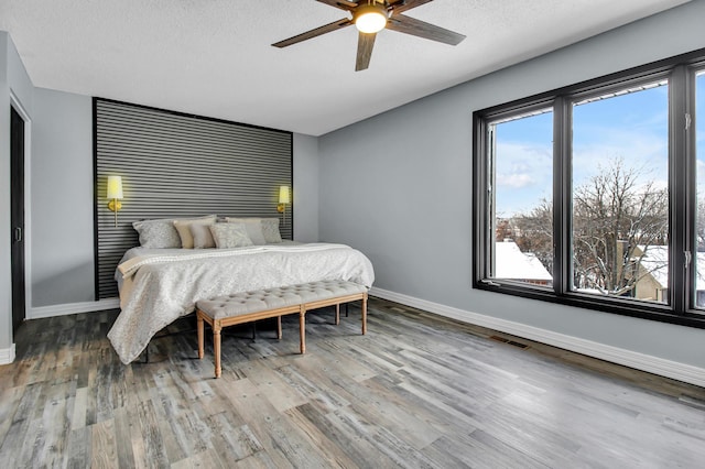 bedroom with visible vents, ceiling fan, a textured ceiling, wood finished floors, and baseboards