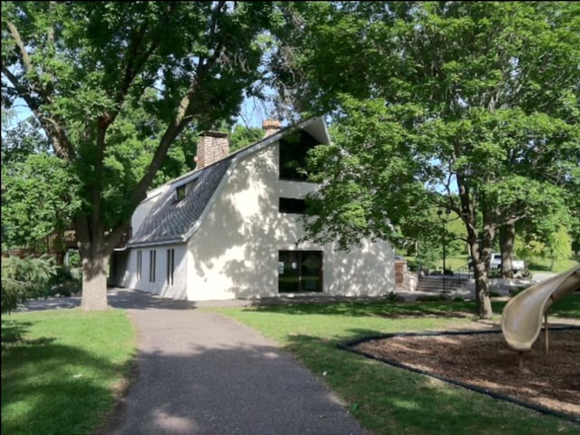 view of home's exterior with a yard, driveway, a chimney, and a gambrel roof