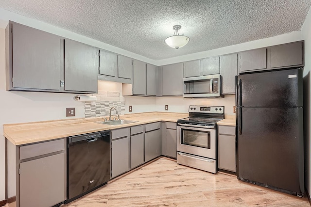 kitchen featuring sink, tasteful backsplash, light hardwood / wood-style flooring, gray cabinets, and black appliances