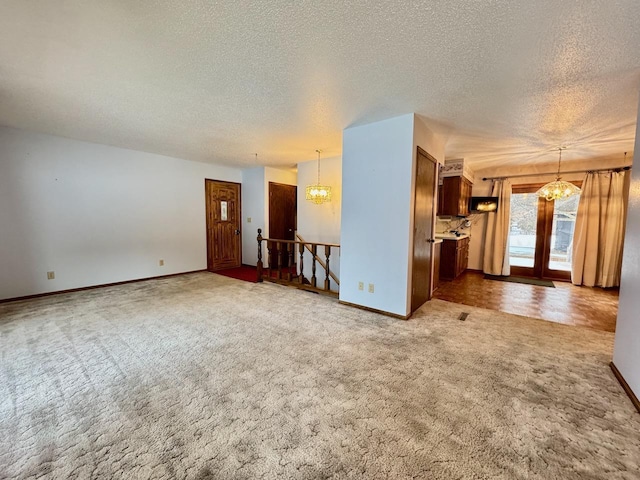 unfurnished living room featuring carpet, french doors, a textured ceiling, and a notable chandelier