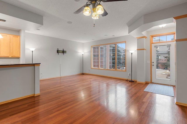 unfurnished living room with a ceiling fan, a textured ceiling, baseboards, and wood finished floors