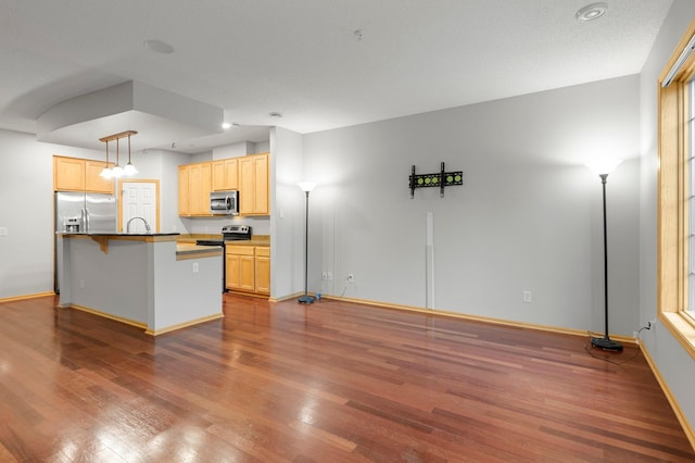 kitchen featuring dark wood-style floors, pendant lighting, appliances with stainless steel finishes, light brown cabinets, and a kitchen breakfast bar