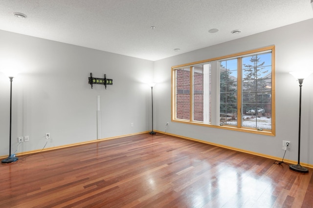 unfurnished room with a textured ceiling, baseboards, and wood finished floors