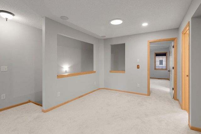 spare room featuring light carpet, a textured ceiling, and baseboards