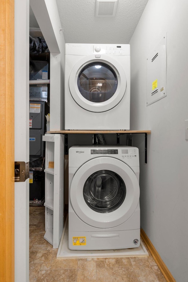 laundry room featuring stacked washer and dryer, visible vents, a textured ceiling, laundry area, and baseboards