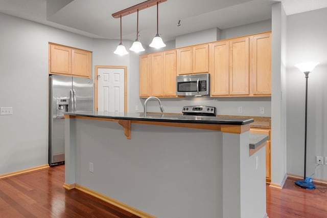 kitchen with decorative light fixtures, a center island with sink, light brown cabinetry, appliances with stainless steel finishes, and dark wood-type flooring