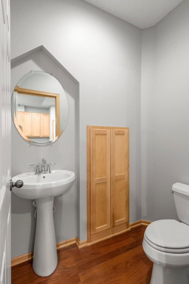 half bath with a sink, wood finished floors, toilet, and baseboards