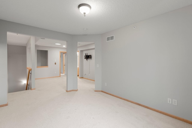 empty room featuring a textured ceiling, carpet flooring, visible vents, and baseboards